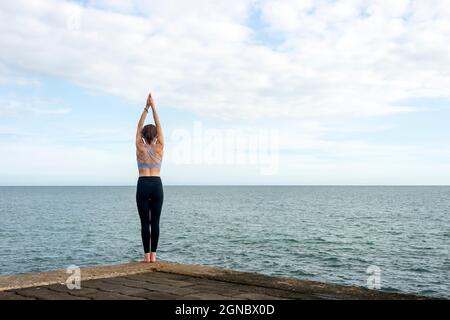 Lo yoga pone, donna che fa tadasana vicino al mare. Foto Stock