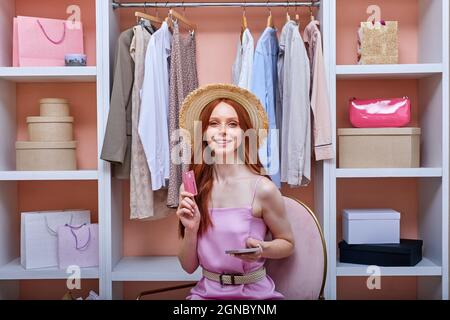 Donna redhead fare shopping online, ordinare la consegna tramite smartphone. lady effettua acquisti online con carta di credito carta di credito relax su sedia a casa interno Foto Stock