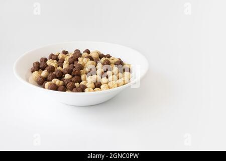 cereali al cioccolato alla vaniglia in ciotola isolata su sfondo bianco, palline di cioccolato marrone e bianco, colazione sana Foto Stock