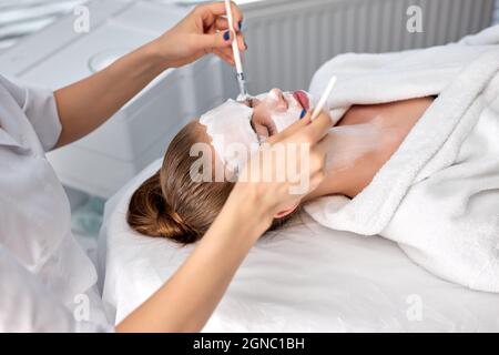 Giovane donna croppata cosmetologist applicare la maschera di argilla bianca sul volto della donna. Bella donna cliente caucasica in salone di bellezza ottenere procedure spa, pulizia Foto Stock