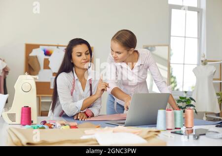 Due donne che hanno un'attività di dressmaking utilizzando un computer portatile mentre lavorano nel loro atelier Foto Stock