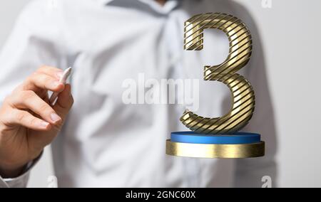 Mano dell'uomo con una penna che punta a un 3d reso dorato 3 su un piedistallo Foto Stock