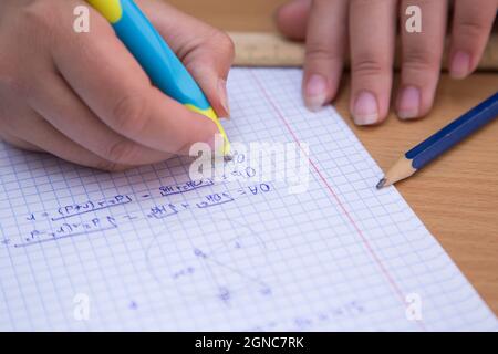 La mano della pupilla in primo piano risolve un problema geometrico in un notebook. Uno scolaro svolge un compito sul posto di lavoro. Il concetto di educazione dei bambini, di insegnamento delle conoscenze, delle competenze e delle abilità. Foto Stock