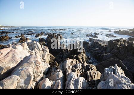 Creste frastagliate che conducono verso il mare e onde che si infrangono sulla riva a De Kelders Foto Stock