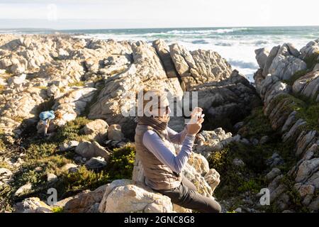 Donna in piedi tra le rocce frastagliate e piscine di roccia sulla costa, scattando foto, Foto Stock