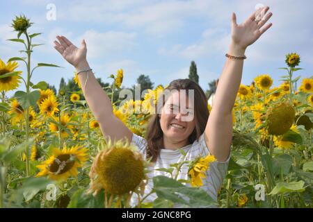 Donna gioiosa con le braccia tese nell'aria, in piedi in un campo di girasole Foto Stock