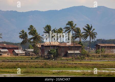 Una piccola città in lontananza, sulle rive del lago Inle, tra risaie e paesaggi paludosi, inondato di acqua, Stato Shan, Birmania, Myanmar Foto Stock