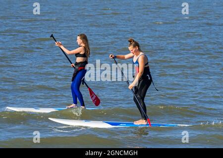 Due pedalò femmina che praticano lo sport acquatici, lo stand up paddleboard / stand up paddleboard / SUP lungo la costa del Mare del Nord Foto Stock