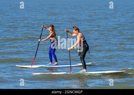 Due pedalò femmina che praticano lo sport acquatici, lo stand up paddleboard / stand up paddleboard / SUP lungo la costa del Mare del Nord Foto Stock