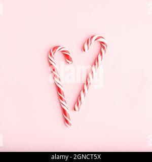 Caramelle dure a forma di cuore a strisce rosse e bianche di Natale su sfondo rosa. Stile a disposizione piatta. Foto Stock