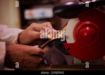 Un paio di mani esperte uomo affilare uno scalpello per lavorazione del legno su una mola da banco. Foto Stock