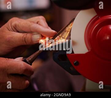 Un paio di mani esperte uomo affilare uno scalpello per lavorazione del legno su una mola da banco. Foto Stock