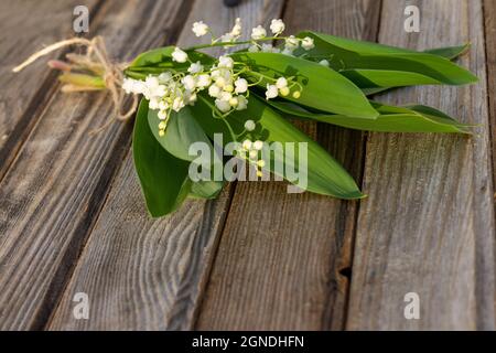 Fiori parzialmente sfocati su una rustica vecchia superficie di legno. Un bouquet di gigli della valle sulle tavole. Spazio di copia Foto Stock