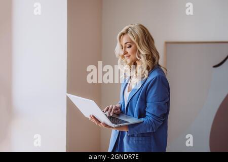 Una bella donna freelance, blogger, influencer con un laptop in mano lavora da remoto. Messa a fuoco selettiva soft. Foto Stock