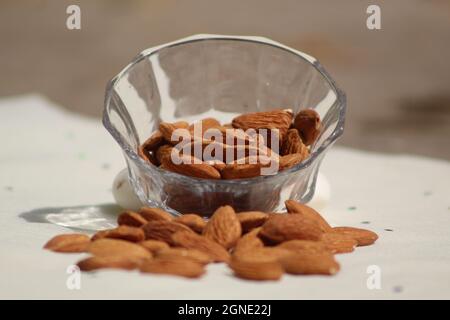 Mandorle che cadono dalla ciotola di vetro su sfondo bianco Foto Stock