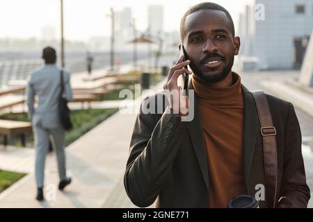 Orizzontale vita su ritratto del giovane africano americano uomo indossare abiti alla moda passeggiando per strada parlando al telefono Foto Stock