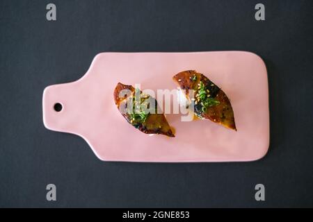 Sushi Giapponese - due sushi Unagi nigiri su tavola rosa chiaro. Pezzi di sushi serviti su ardesia puntina-luce isolato su sfondo nero. Sushi con anguilla sul retro Foto Stock