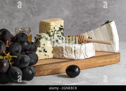 Camembert, Roquefort e brie con miele, uva e noci sul tagliere. Foto Stock
