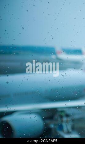 La pioggia cade sulla finestra pulita dell'edificio del terminal dell'aeroporto con aerei defocused sul grembiule di sfondo in una giornata buia Foto Stock