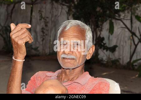 Primo piano di un agricoltore indiano e vecchio uomo seduto nel cortile della casa con il viso sorridente e felice la sera Foto Stock