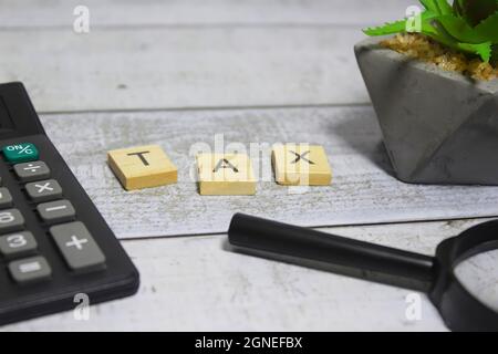 Parola di imposta scritta su blocco di legno e circondata da calcolatrice e lente d'ingrandimento. Messa a fuoco selettiva. Foto Stock