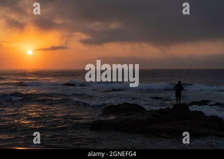 Lone pescatore sulle rocce durante la bella alba sulla spiaggia. Durban, East Coast, Sudafrica. Foto di alta qualità Foto Stock