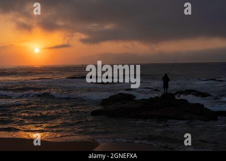 Lone pescatore sulle rocce durante la bella alba sulla spiaggia. Durban, East Coast, Sudafrica. Foto di alta qualità Foto Stock