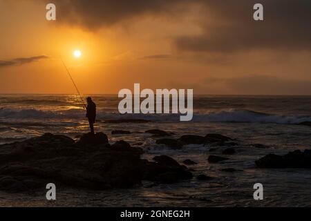 Lone pescatore sulle rocce durante la bella alba sulla spiaggia. Durban, East Coast, Sudafrica. Foto di alta qualità Foto Stock