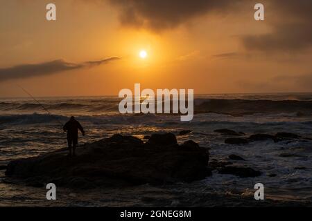 Lone pescatore sulle rocce durante la bella alba sulla spiaggia. Durban, East Coast, Sudafrica. Foto di alta qualità Foto Stock