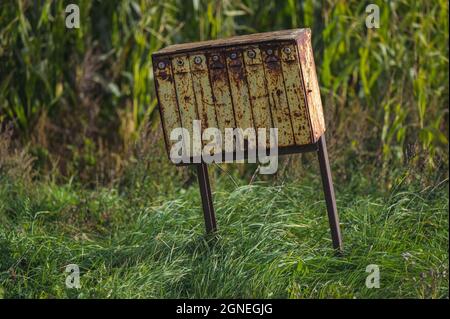 una vecchia cassetta postale gialla arrugginita da un campo di mais in una giornata di sole e una lunga erba che ondeggiano nel vento sotto la cassetta postale Foto Stock