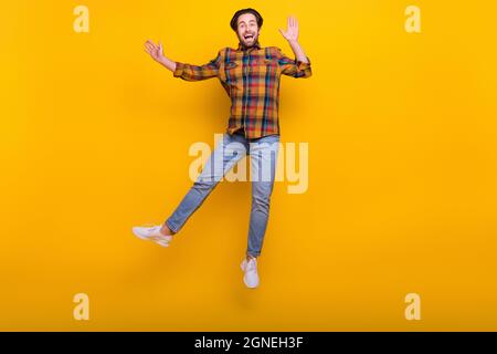 Foto a tutta lunghezza di divertente brunet millennial ragazzo salto indossare camicia jeans sneakers isolato su sfondo giallo Foto Stock