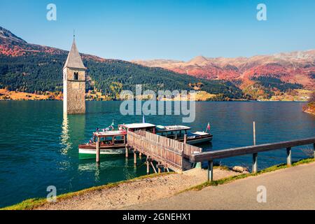 Splendida vista autunnale della Torre della chiesa sunken nel lago di Resia. Scena mattutina di sole delle Alpi italiane, Alto Adige, Italia, Europa. Concetto di viaggio indietro Foto Stock