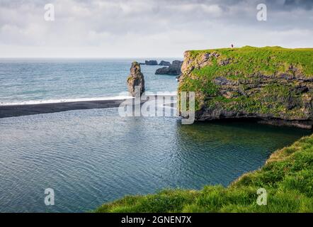 Pittoresca alba estiva nella Riserva Naturale di Dyrholaey con l'uomo solitario sulla roccia. Grande vista dell'arco di Dyrholaey, costa meridionale dell'Islanda, Europa. Inst Foto Stock