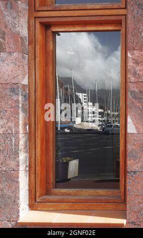 Il riflesso su una vetrina dove si vede il porto, le montagne, il cielo, le barche, nel porto di San Sebastian, Isole Canarie Foto Stock