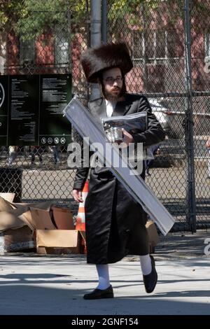 A Sukkos, un ebreo ortodosso cammina dalla sinagoga portando un esrog & lulav e indossando uno shtreimel. A Williamsburg, Brooklyn, New York. Foto Stock