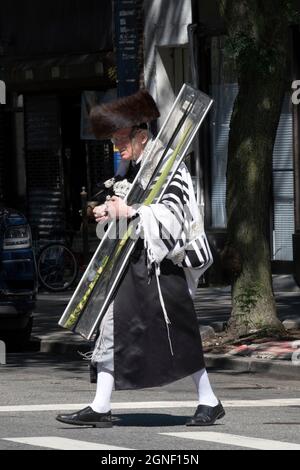 A Sukkos, un ebreo ortodosso cammina dalla sinagoga portando un esrog & lulav e indossando uno shtreimel. A Williamsburg, Brooklyn, New York. Foto Stock