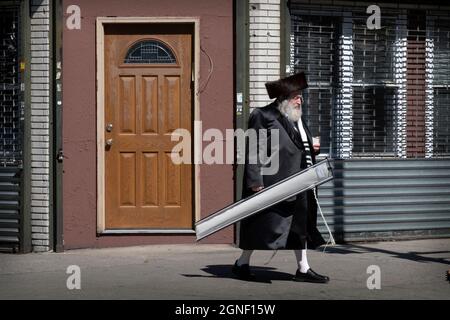 A Sukkos, un ebreo ortodosso cammina dalla sinagoga portando un esrog & lulav e indossando uno shtreimel. A Williamsburg, Brooklyn, New York. Foto Stock