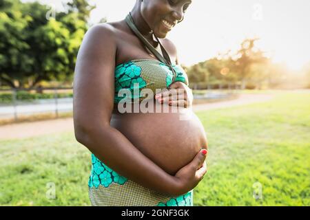 Primo piano ventre incinta di giovane donna africana nel parco durante il tramonto - concetto di stile di vita di maternità Foto Stock