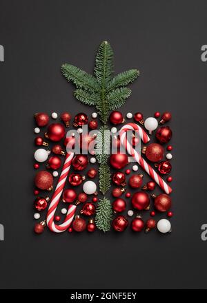 Scheda di Natale concettuale con scatola regalo di festa fatta da un bastone della caramella, palle di Natale e rami dell'albero di abete su sfondo nero Foto Stock