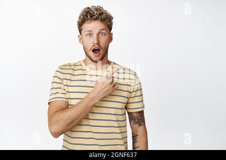 WOW controllare questo fuori. L'uomo bello impressionato punta il dito sul logo, mostra l'annuncio di vendita dell'angolo destro, in piedi in t-shirt su sfondo bianco Foto Stock