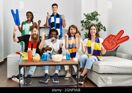 Gruppo di amici che sostengono la squadra di calcio che guarda la tv a casa seduta sul divano urlando orgoglioso, celebrando la vittoria e il successo molto eccitato con r Foto Stock