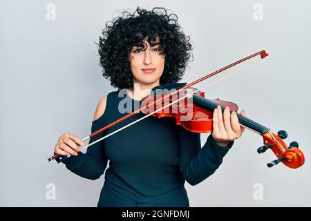 Giovane donna medio-orientale che gioca violino rilassato con espressione seria sul viso. Semplice e naturale guardare la fotocamera. Foto Stock