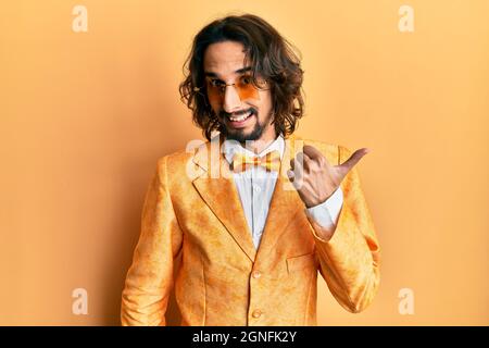 Giovane uomo ispanico che indossa hipster elegante look sorridente con felice volto guardando e puntando al lato con il pollice in su. Foto Stock