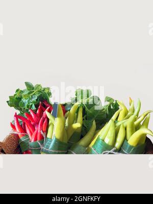 pacchetto di design fresco biologico verde e rosso peperoncino avvolto in foglie di banana con altre verdure isolate in bianco fusto tagliato Foto Stock