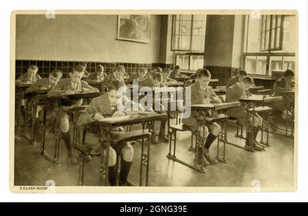 Cartolina originale degli anni '30 di ragazzi junior in classe, ragazzi alla scrittura scrivanie, luogo sconosciuto, Regno Unito Foto Stock