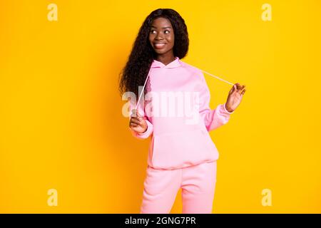 Foto di lucido affascinante pelle scura donna vestita felpa con cappuccio rosa guardando spazio vuoto isolato colore giallo sfondo Foto Stock