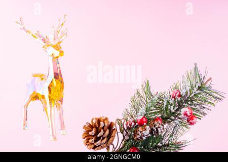 Decoro di Natale figurine cervo e un ramo di abete rosso nella neve su uno sfondo rosa. Composizione natalizia con cervi giocattolo olografico. Fe Foto Stock