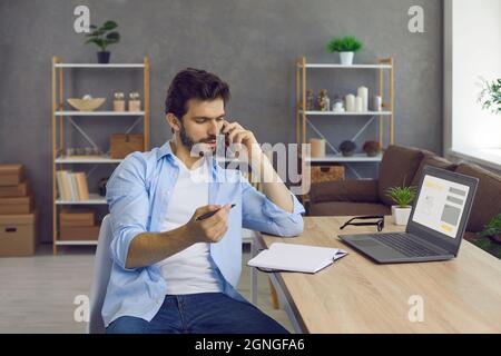 Serio giovane imprenditore ha una conversazione di affari al telefono e prende appunti. Foto Stock