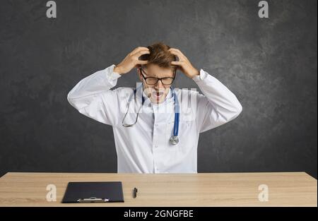Ritratto di giovane medico maschio infuriato in stress urlando forte afferrare la testa. Foto Stock