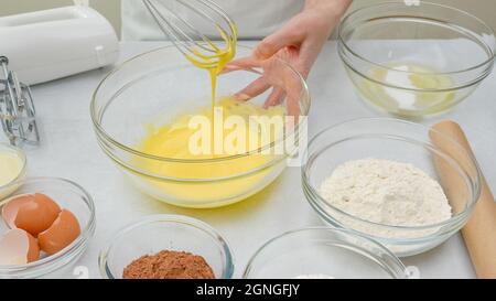 Sbattere i tuorli d'uovo con lo zucchero in un recipiente di vetro. Passo dopo passo ricetta torta al cioccolato, primo piano processo di preparazione, mani donna Foto Stock